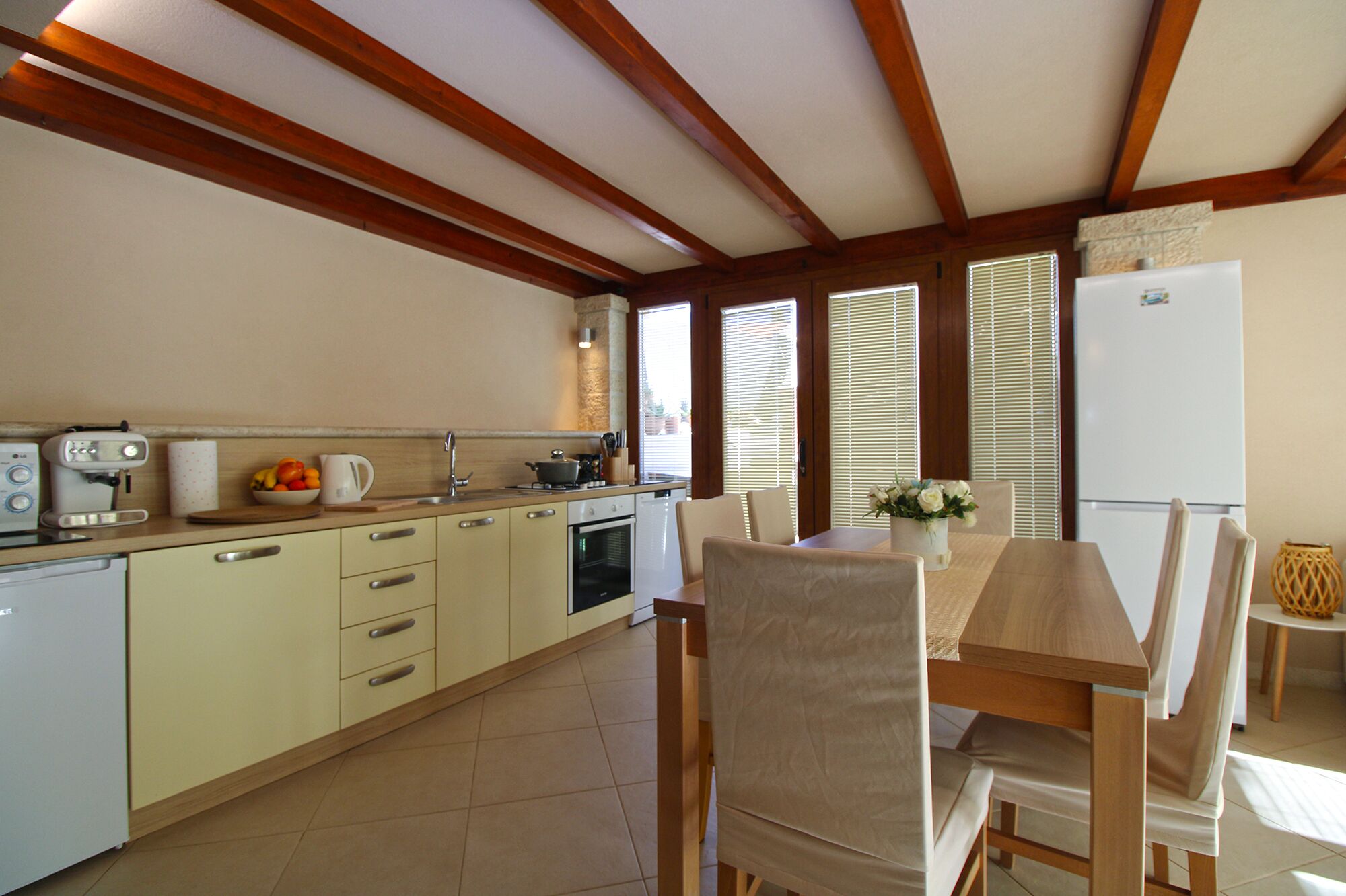 A kitchen with a dining area, wooden beams on the ceiling, a refrigerator, and a coffee maker.