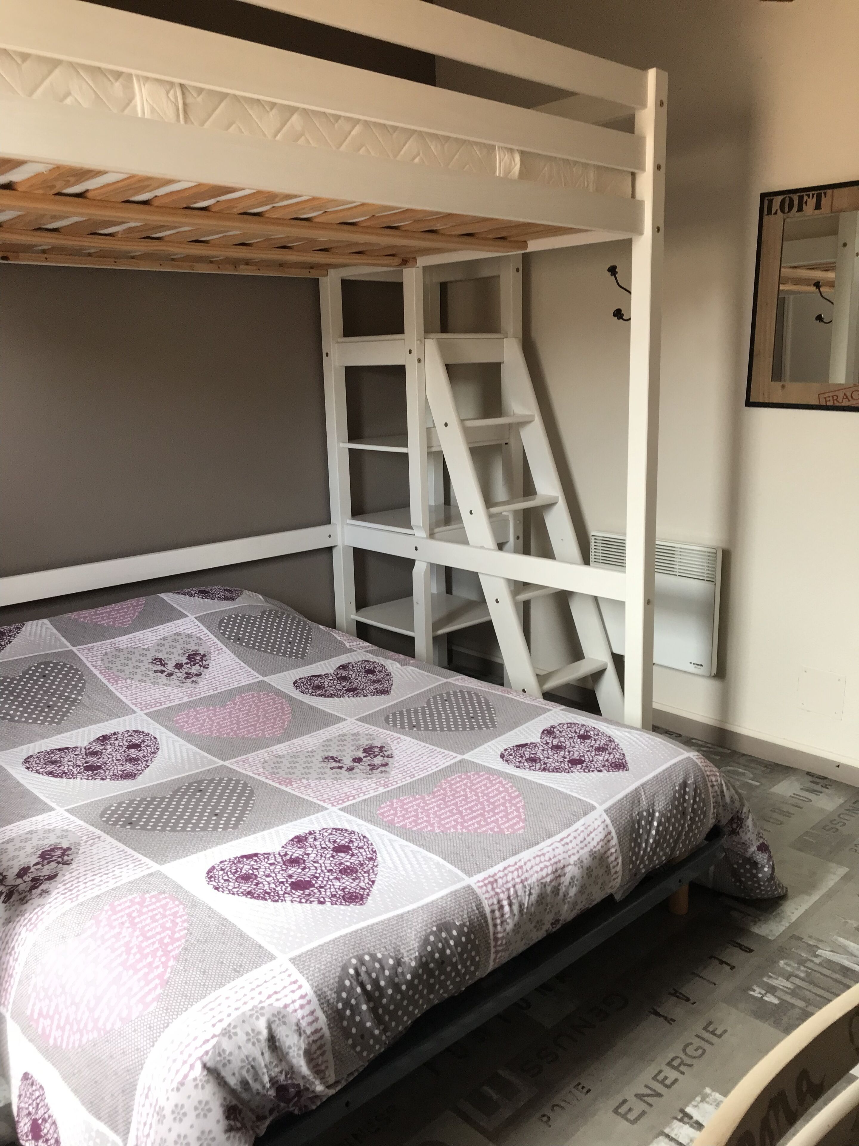 A bunk bed with a ladder, a quilt with heart patterns, and a wall-mounted air conditioner.