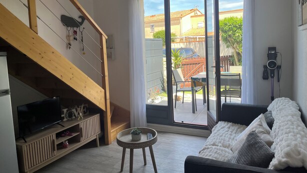 A living room with a TV, wooden staircase, sliding glass door, and a sofa. - Air-conditioned house with pool, bikes and terrace 800 metres from the beach (Saint-Cyprien Plage)