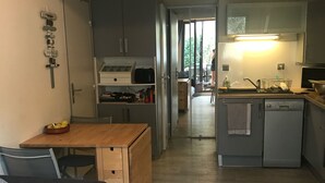 A compact living space with a sofa, a small dining table, a kitchenette, and a visible door leading to a balcony. - Air-conditioned house with pool, bikes and terrace 800 metres from the beach (Saint-Cyprien Plage)