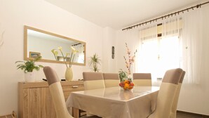 A dining area with a table set for four, surrounded by chairs, a wooden cabinet, and a mirror on the wall.