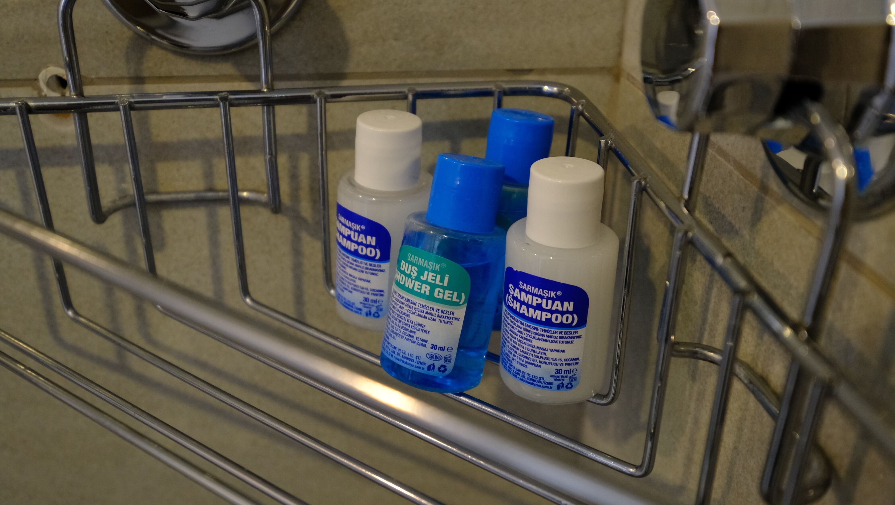 A metal shelf with three bottles of shampoo and conditioner in a bathroom setting.