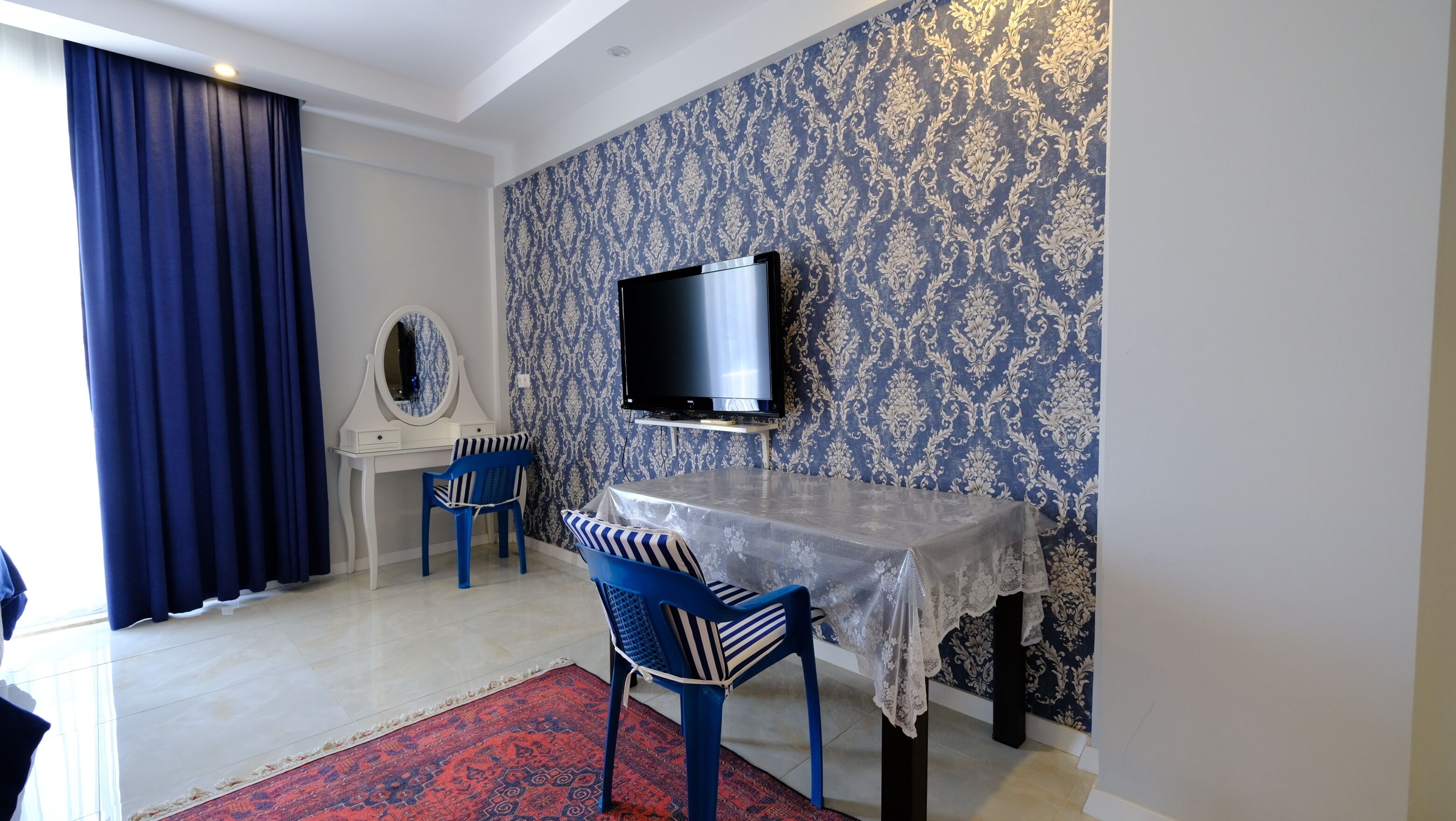Una habitación con televisión montada en la pared, un escritorio con silla, y un papel tapiz estampado.