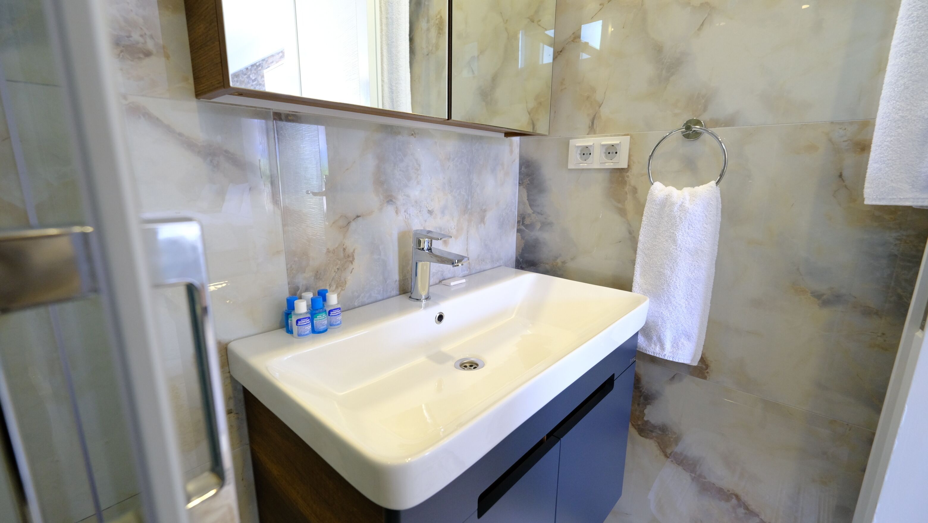 Un baño con un lavamanos blanco, un espejo y un perchero para toallas.