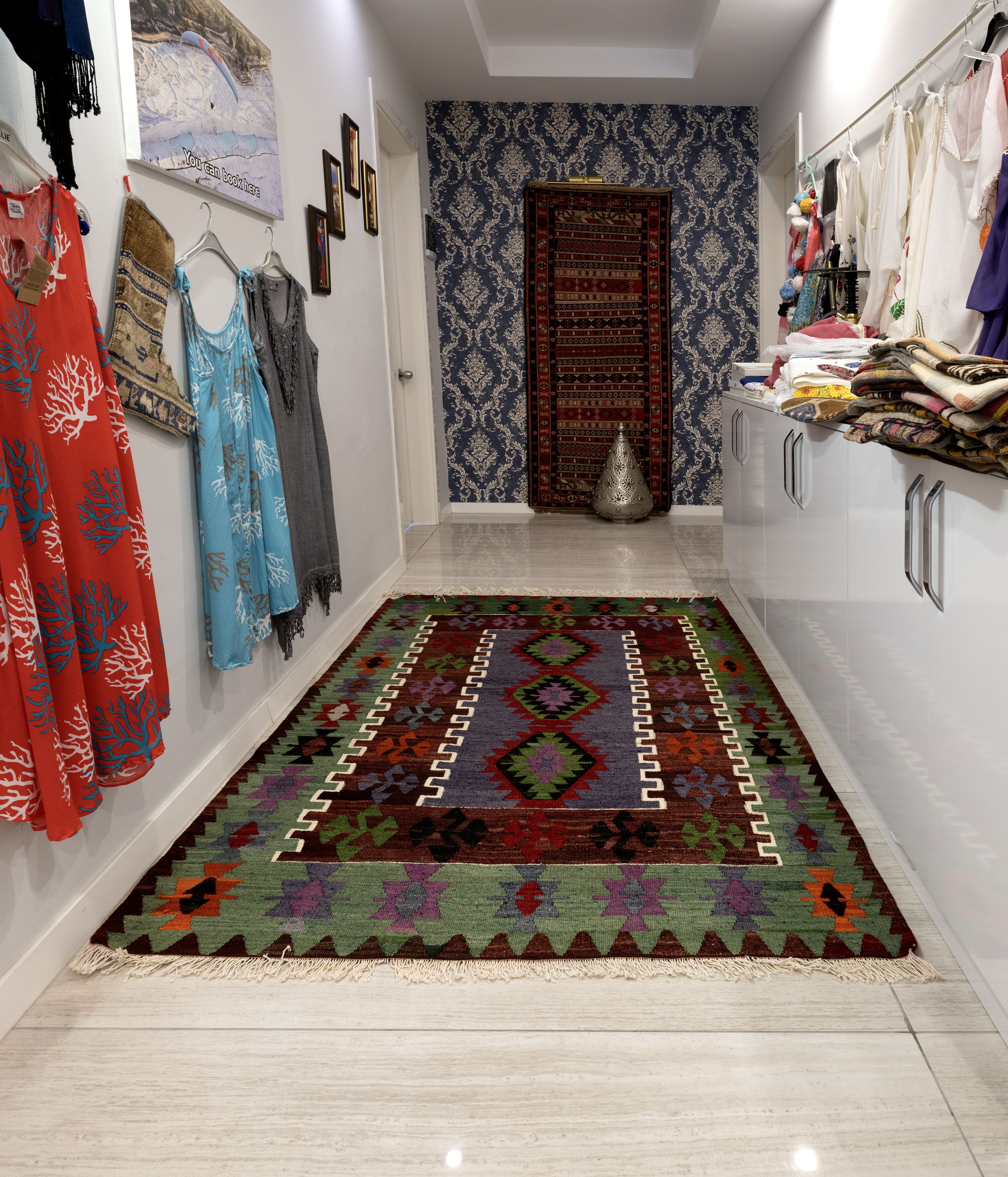 A hallway with a patterned rug, a wardrobe with hanging clothes, and a decorative door.