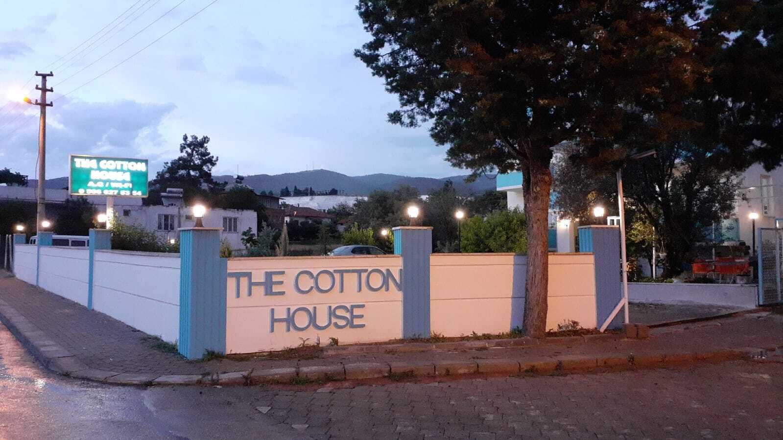 A sign for "The Cotton House" with a paved entrance and a tree to the right.
