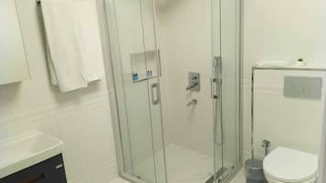 A modern bathroom with a glass-enclosed shower, a toilet, and a sink.