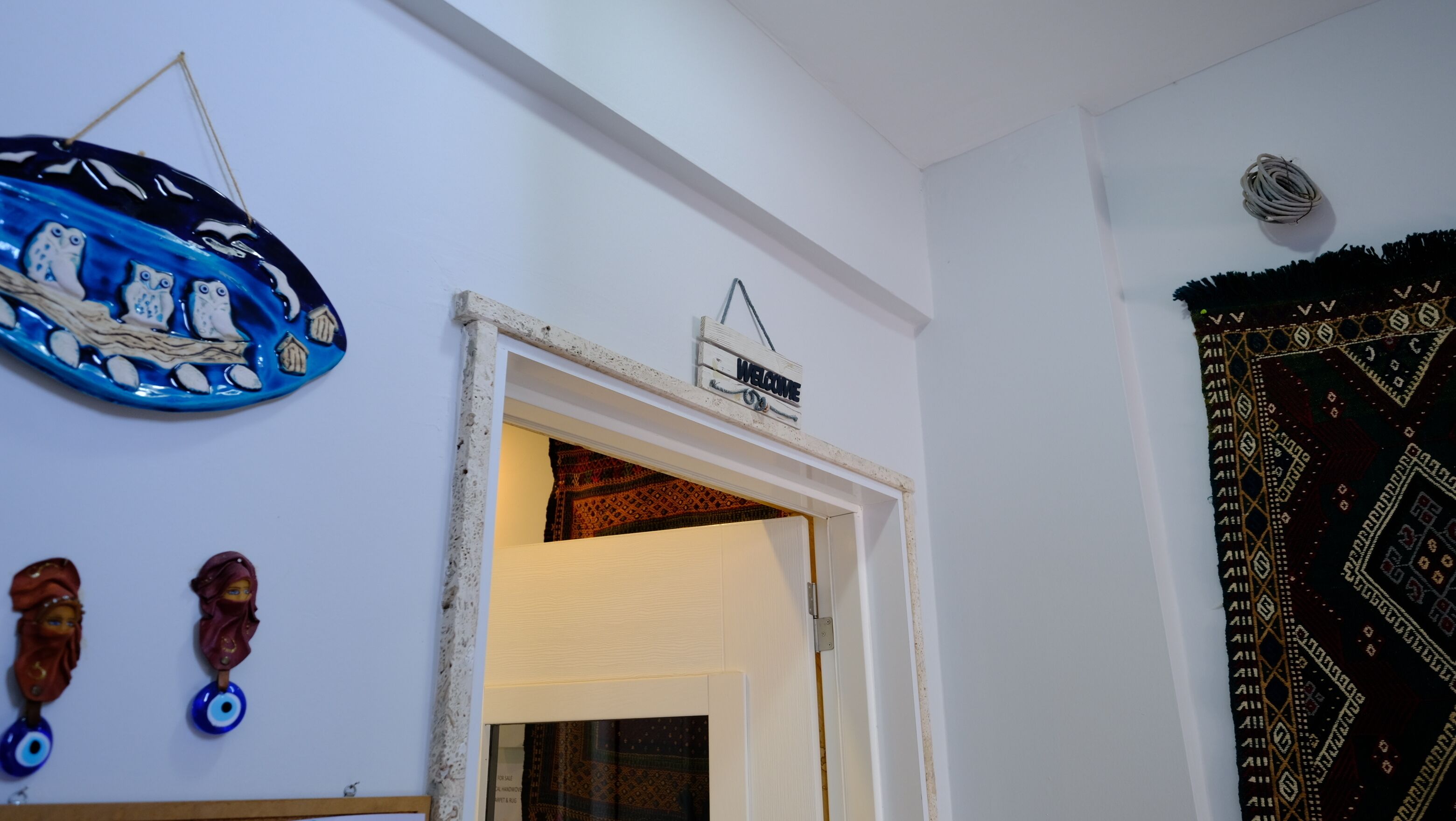 A doorway with a 'Welcome' sign, a patterned tapestry, and decorative items on the wall.