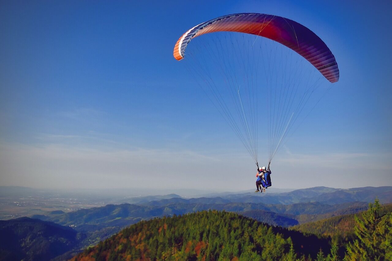 A person paragliding over a mountainous landscape with dense forests below.
