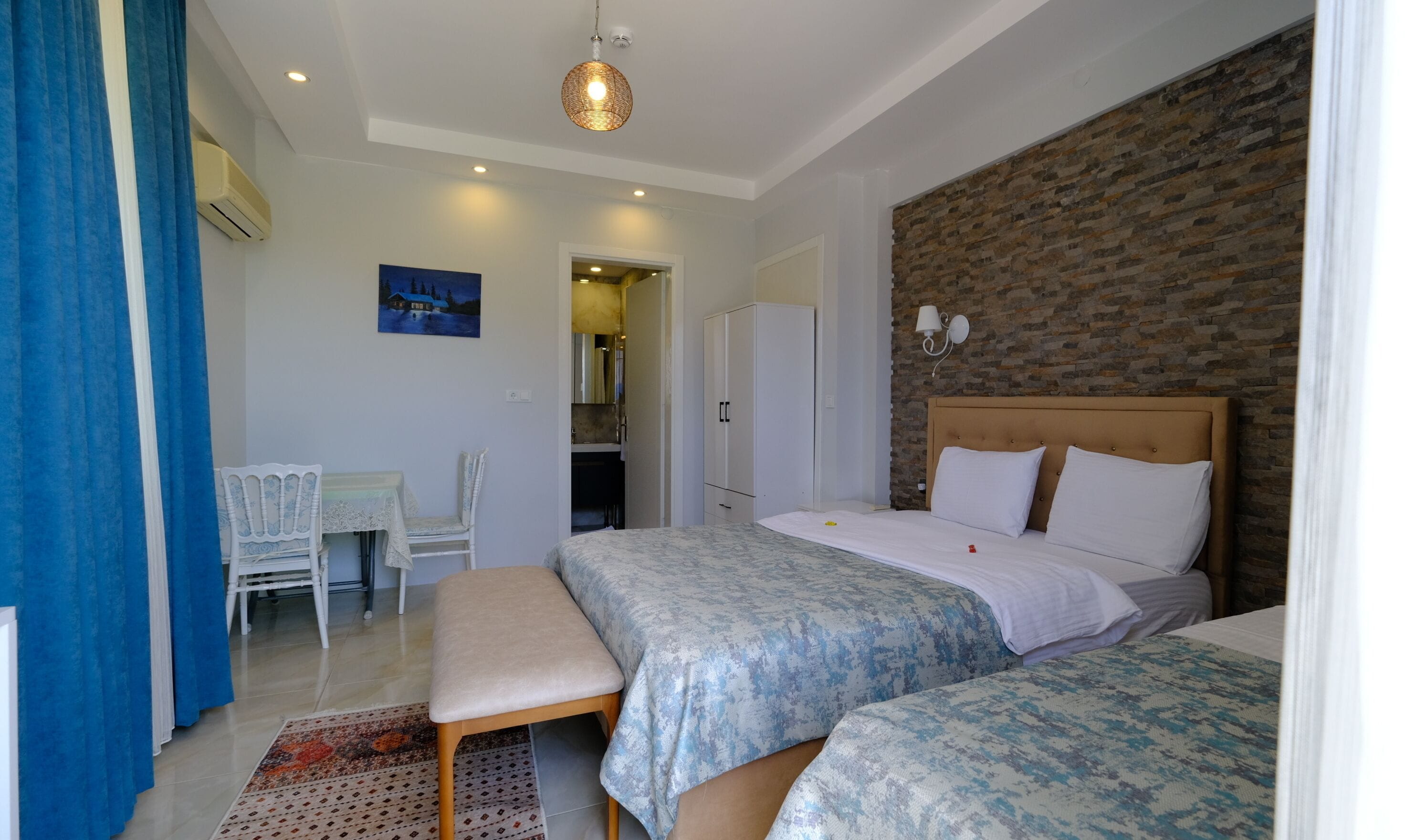 Habitación de hotel con dos camas, un escritorio y una silla. Hay un cuadro en la pared y una pared decorativa de ladrillo.