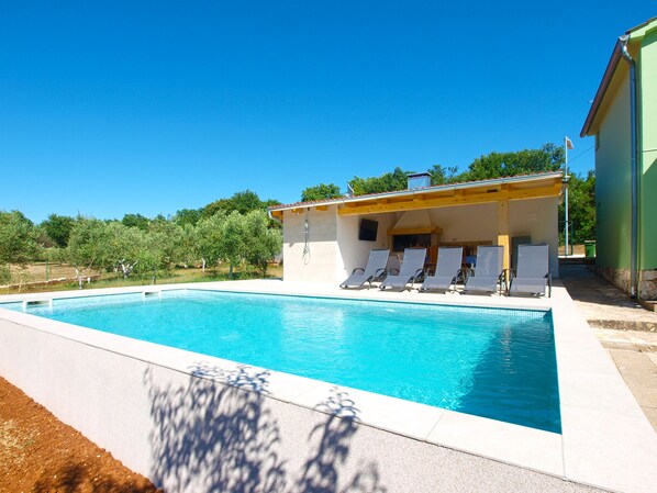 A swimming pool with lounge chairs and a covered area with a wooden roof.