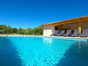 Une piscine d’un bleu éclatant, dotée de chaises longues et d’un espace abrité.