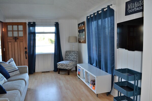 Een gezellige woonkamer met een houten deur, een gestreept fauteuil, een witte console tafel en een aan de muur bevestigde televisie.