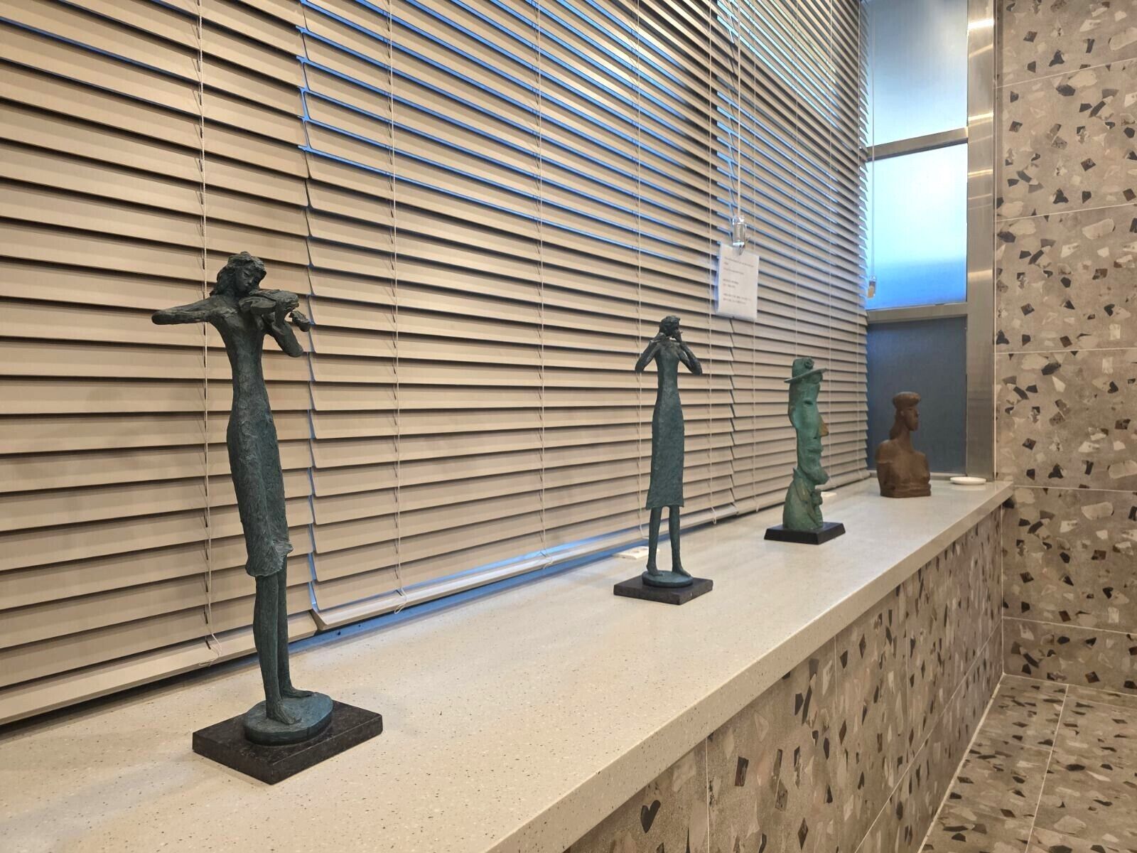 A corridor with a series of bronze sculptures on a counter, a window with blinds, and a patterned wall.