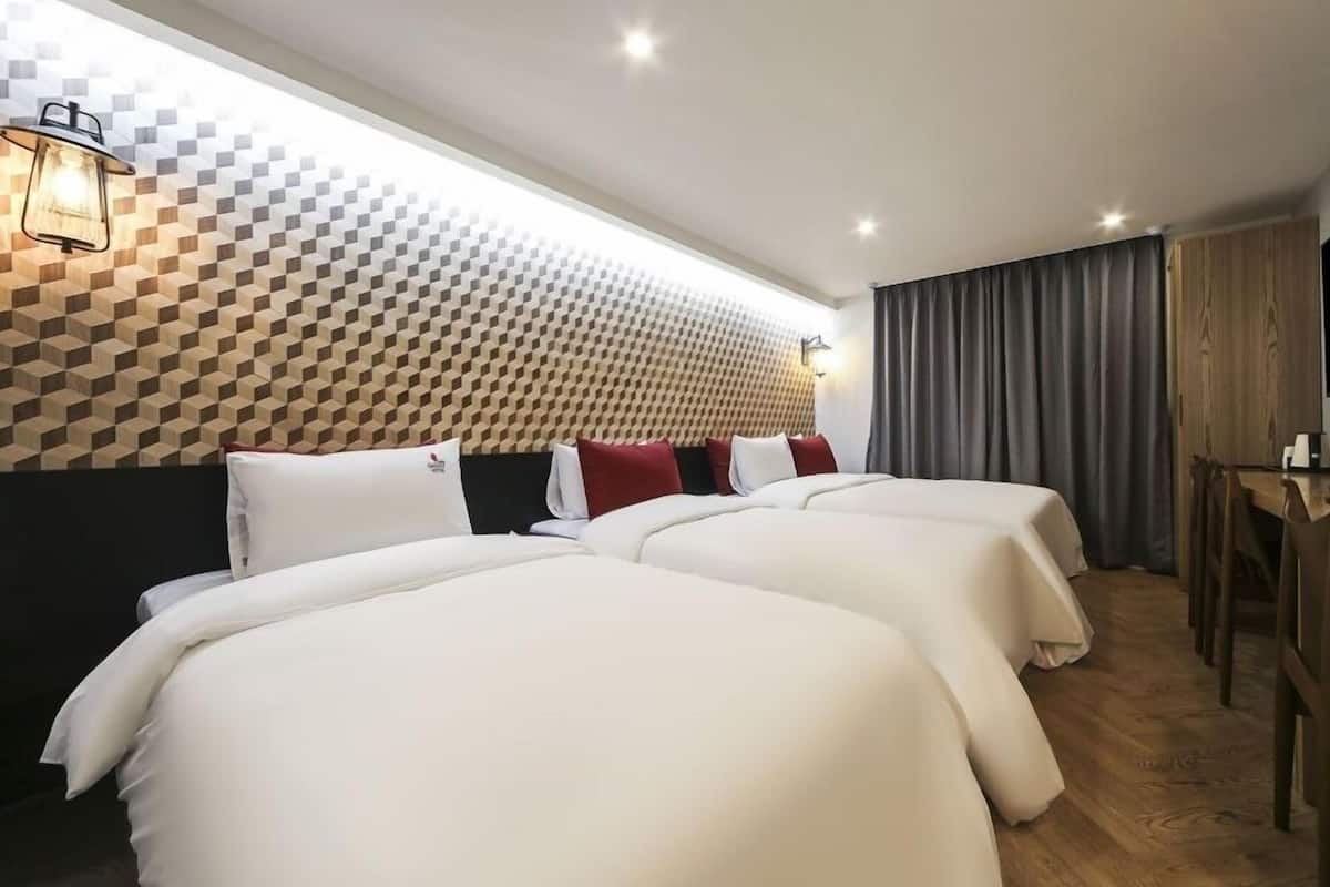 A hotel room with two beds, a wooden desk, a flat-screen TV, and a patterned wall.