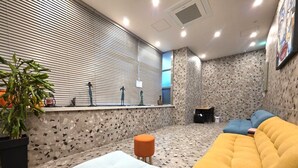 A modern lounge area with a patterned floor, a seating area with a yellow sofa and a light-colored ottoman, a small table with a chair, and a potted plant. - Busan Maron Hotel Nampo (Busan)