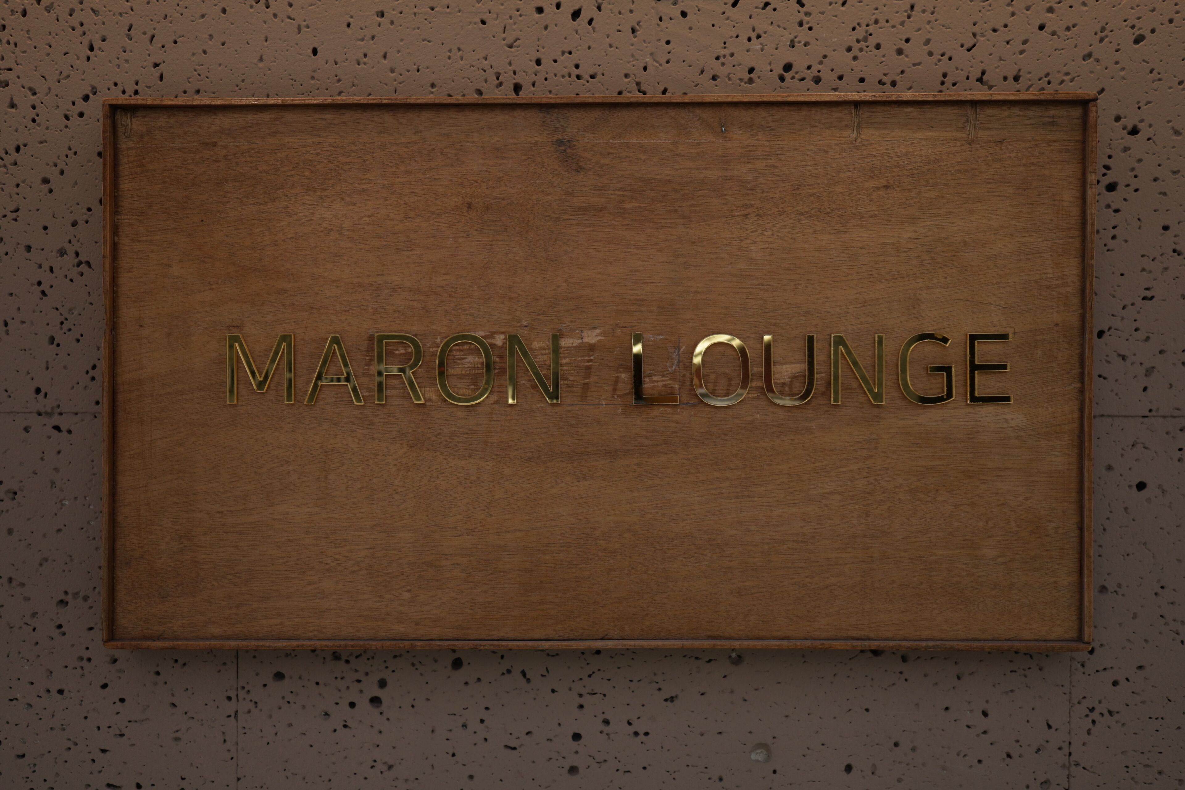 Un letrero de madera con el texto 'Maron Lounge' colocado sobre una pared moteada.