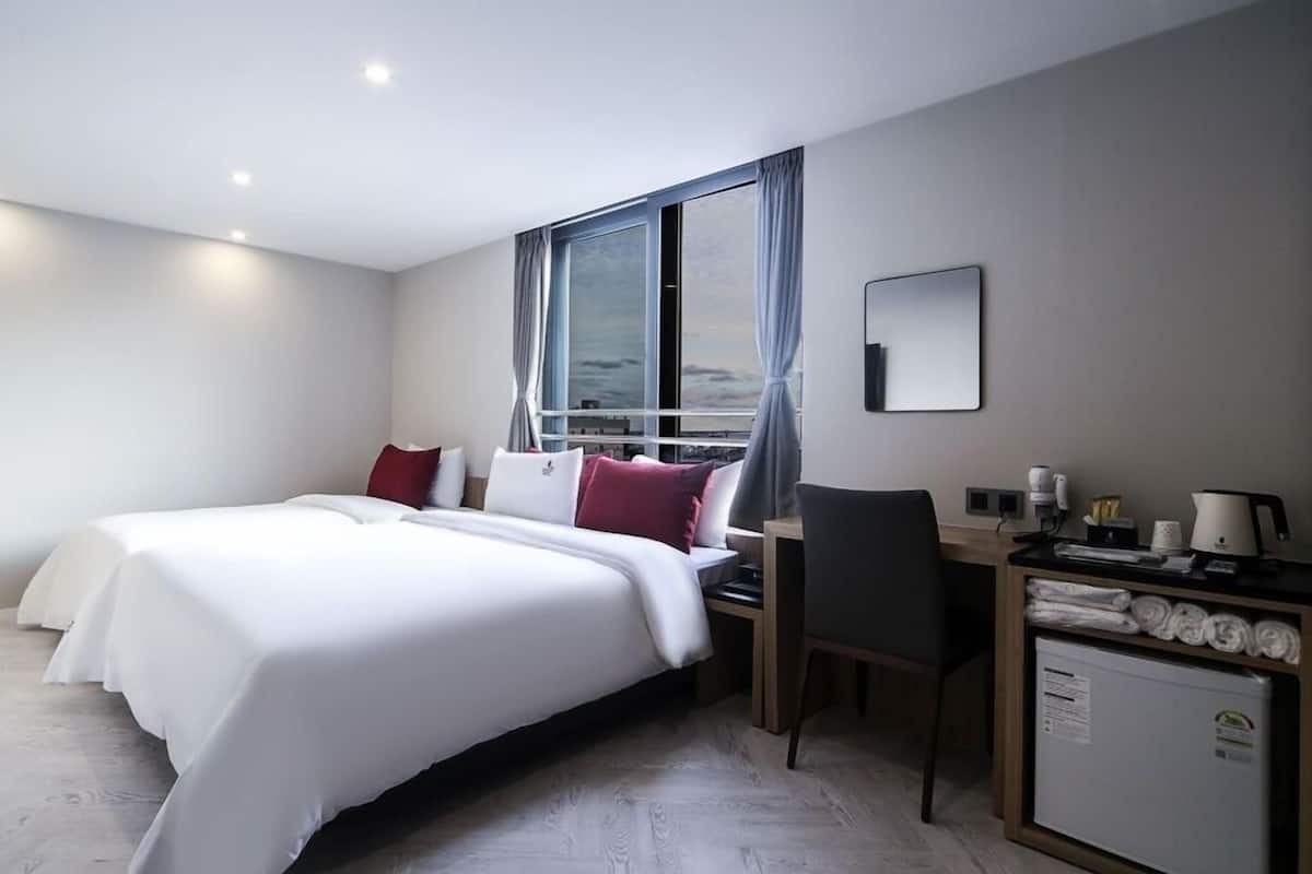A modern hotel room with a large bed, a desk, and a view of the city through the window.