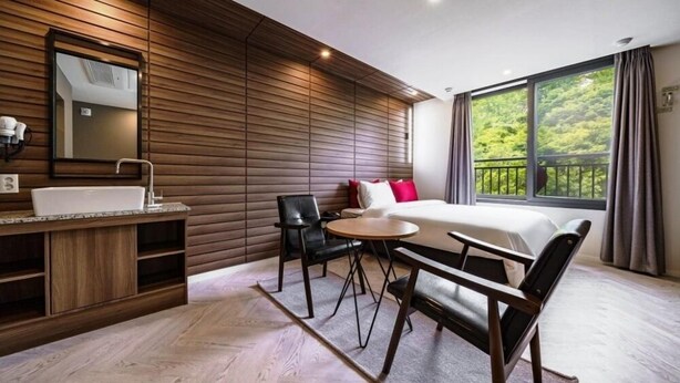 A modern hotel room with a wooden wall, a large window with a view, a bed, a desk, and a chair. - Busan Maron Hotel Nampo (Busan)