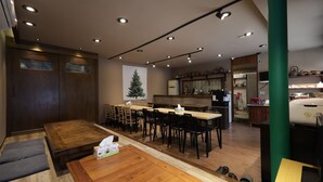 A restaurant with wooden tables and chairs, a kitchen area, and a green pillar. - Busan Maron Hotel Nampo (Busan)