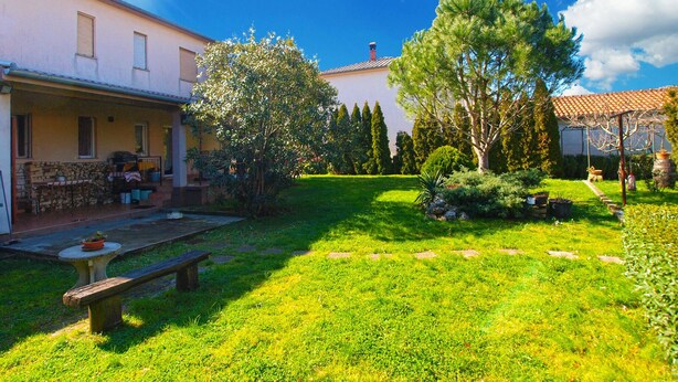 A sunny courtyard with a stone bench, a table with a bowl, and a covered area with a pergola.