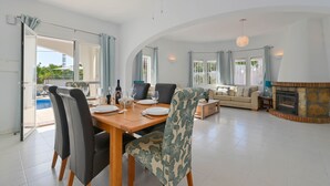 A spacious living area with a dining table, chairs, a sofa, a fireplace, and a pool visible through the glass doors. - Charlotte - Benissa, Costa Blanca (Benissa)