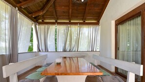 A covered patio with a wooden table and benches, large windows with curtains, and a view of greenery. - Apartment 1561/15973 (Istria - Žminj), 20000m from the beach (Žminj)