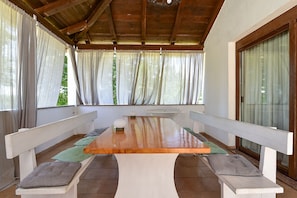 A covered patio with a wooden table and benches, large windows with curtains, and a view of greenery. - Apartment 1561/15973 (Istria - Žminj), 20000m from the beach (Žminj)