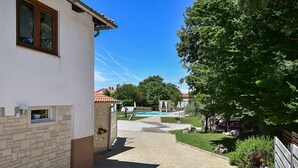 A paved pathway leading to a swimming pool, surrounded by greenery and a building with a window and a wall-mounted light fixture. - Apartment 1561/15973 (Istria - Žminj), 20000m from the beach (Žminj)