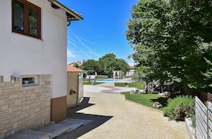 A paved pathway leading to a swimming pool, surrounded by greenery and a building with a window and a wall-mounted light fixture. - Apartment 1561/15973 (Istria - Žminj), 20000m from the beach (Žminj)