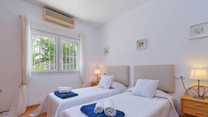 A hotel room with two beds, a window with curtains, a bedside table with a lamp, and a wall-mounted air conditioner. - Modern and comfortable holiday home in Benissa, Costa Blanca, Spain  with private pool for 6 persons (Benissa)