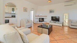 A modern living room with a fireplace, a television, and a kitchen visible through an archway. - Modern and comfortable holiday home in Benissa, Costa Blanca, Spain  with private pool for 6 persons (Benissa)
