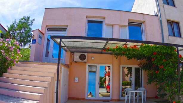 Un edificio de dos plantas con techo plano, un patio cubierto con mobiliario exterior y una escalera que conduce a la entrada.