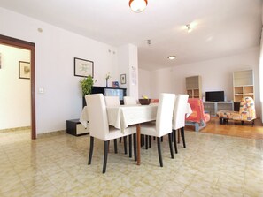 A dining area with a table set for four, surrounded by chairs. There is a television on a stand in the background.