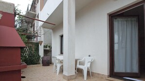 Eine Terrasse mit Tisch und Stühlen, ein großes Fenster und ein rotes Gebäude.