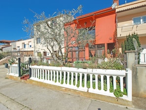A row of Mediterranean-style houses with balconies, a white fence with greenery, and a clear blue sky.