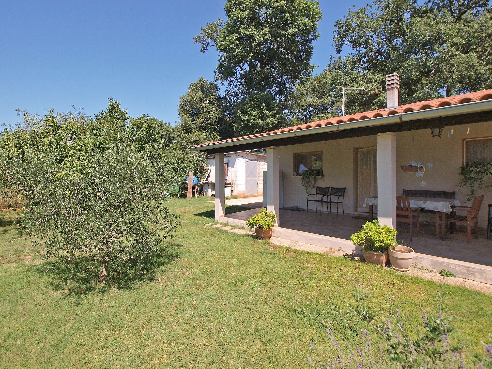 A house with a covered porch, a dining table, and chairs. There are potted plants and a small garden area.