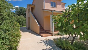 A two-story house with a staircase leading to the entrance, surrounded by greenery.