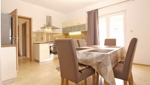 A modern kitchen with a central island, a dining area with a table and chairs, and a view of the outside through a large window.