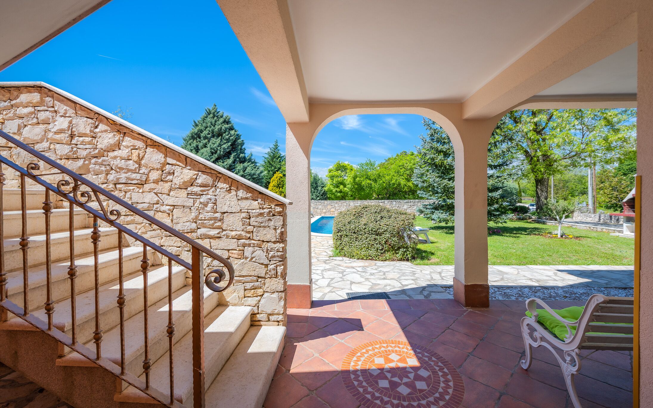 A covered outdoor area with a stone staircase, a pool, and a lawn.
