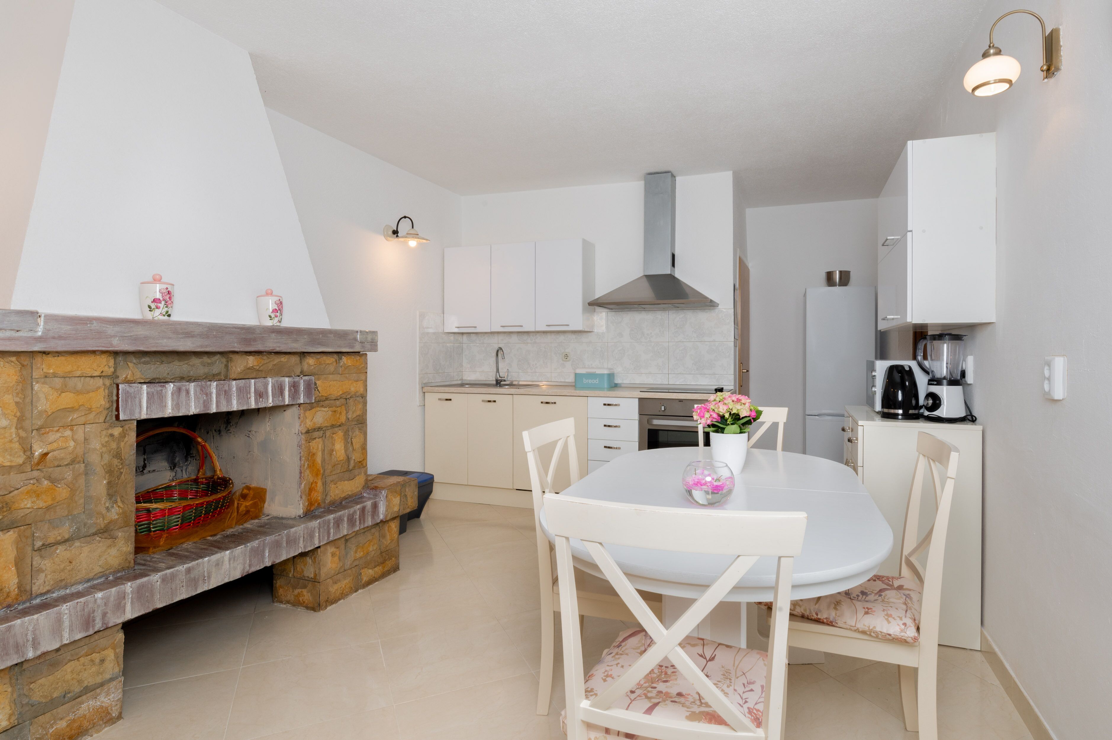 Una cocina moderna con armarios blancos, una chimenea de piedra y un comedor con mesa y sillas blancas.