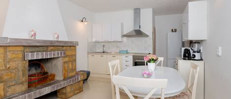 Una cocina moderna con armarios blancos, una chimenea de piedra y un comedor con mesa y sillas blancas.