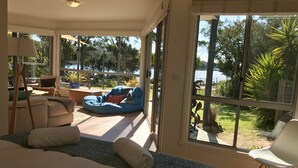 Una habitación amplia con una cama grande, un sillón de peluche azul, una silla blanca y vistas a un lago y vegetación.