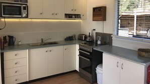 Cocina moderna con armarios blancos, microondas, tetera y ventana con persianas.