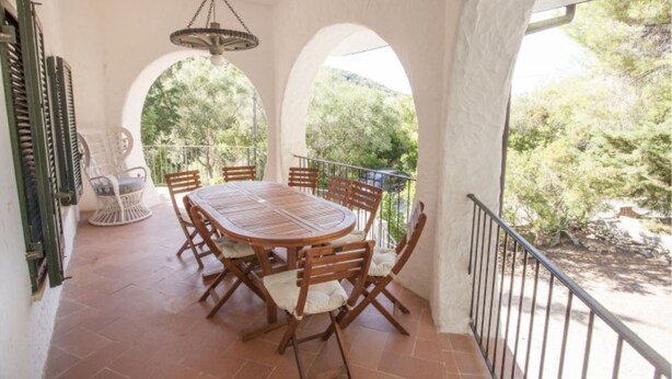 Un espace extérieur abrité, aménagé pour les repas, avec une table ronde et des chaises, le tout entouré d’arches et d’une balustrade.