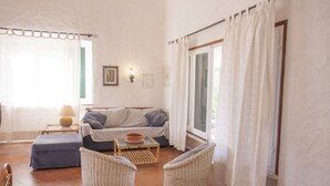 Un salon chaleureux avec un canapé, deux fauteuils en osier, une petite table et une fenêtre avec des rideaux.