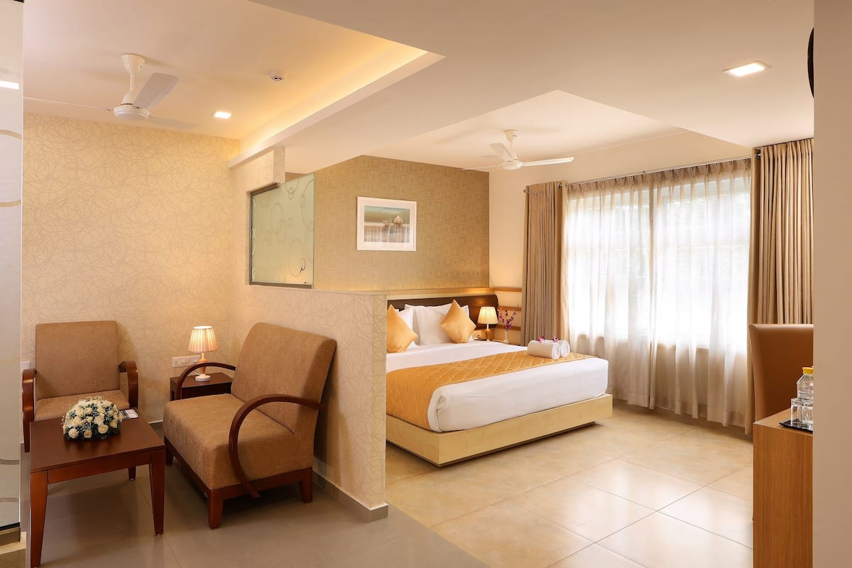 A hotel room with a bed, two armchairs, a desk, a lamp, and a picture on the wall.