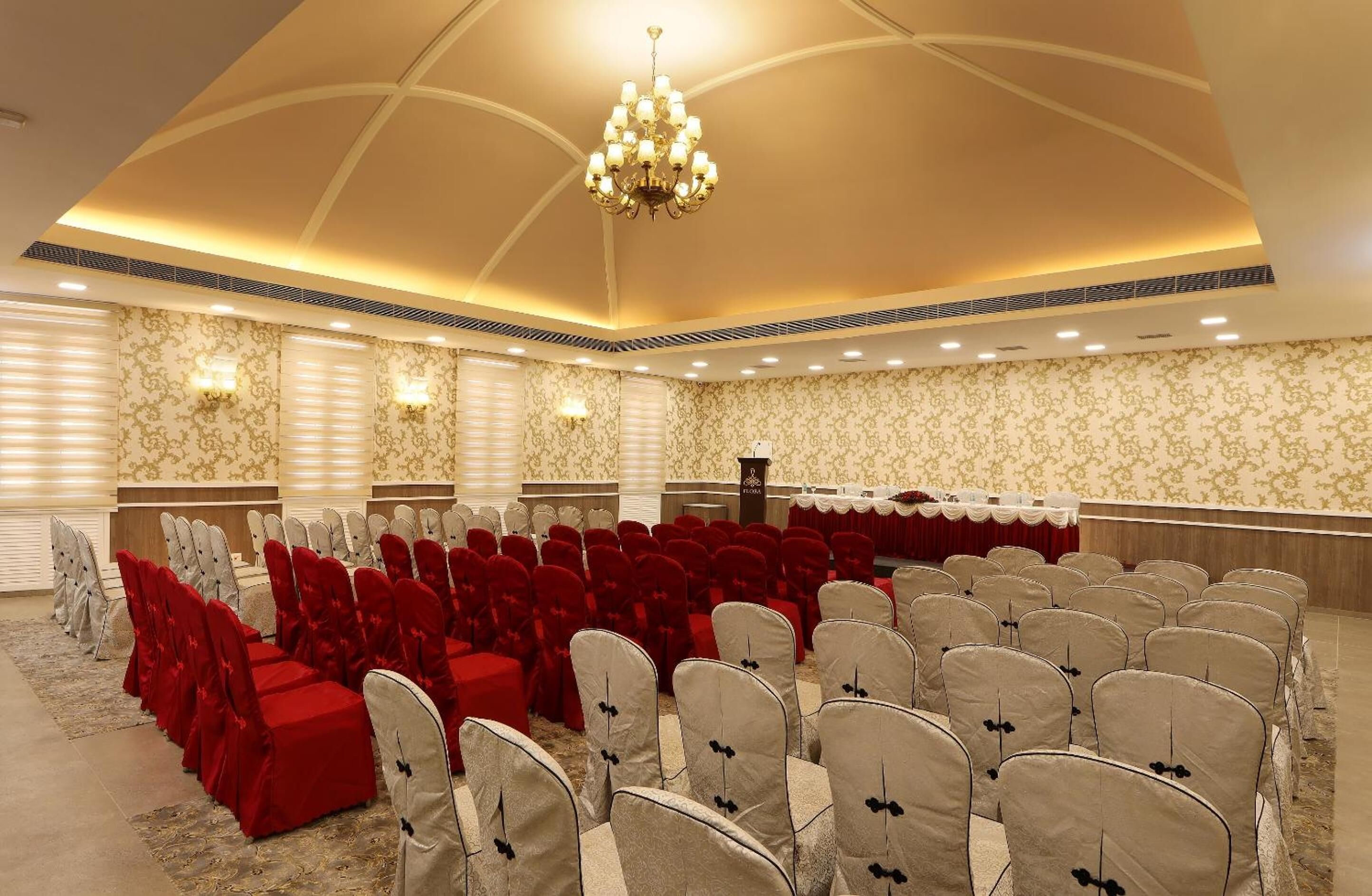 A banquet hall with rows of chairs, a stage, and a chandelier.