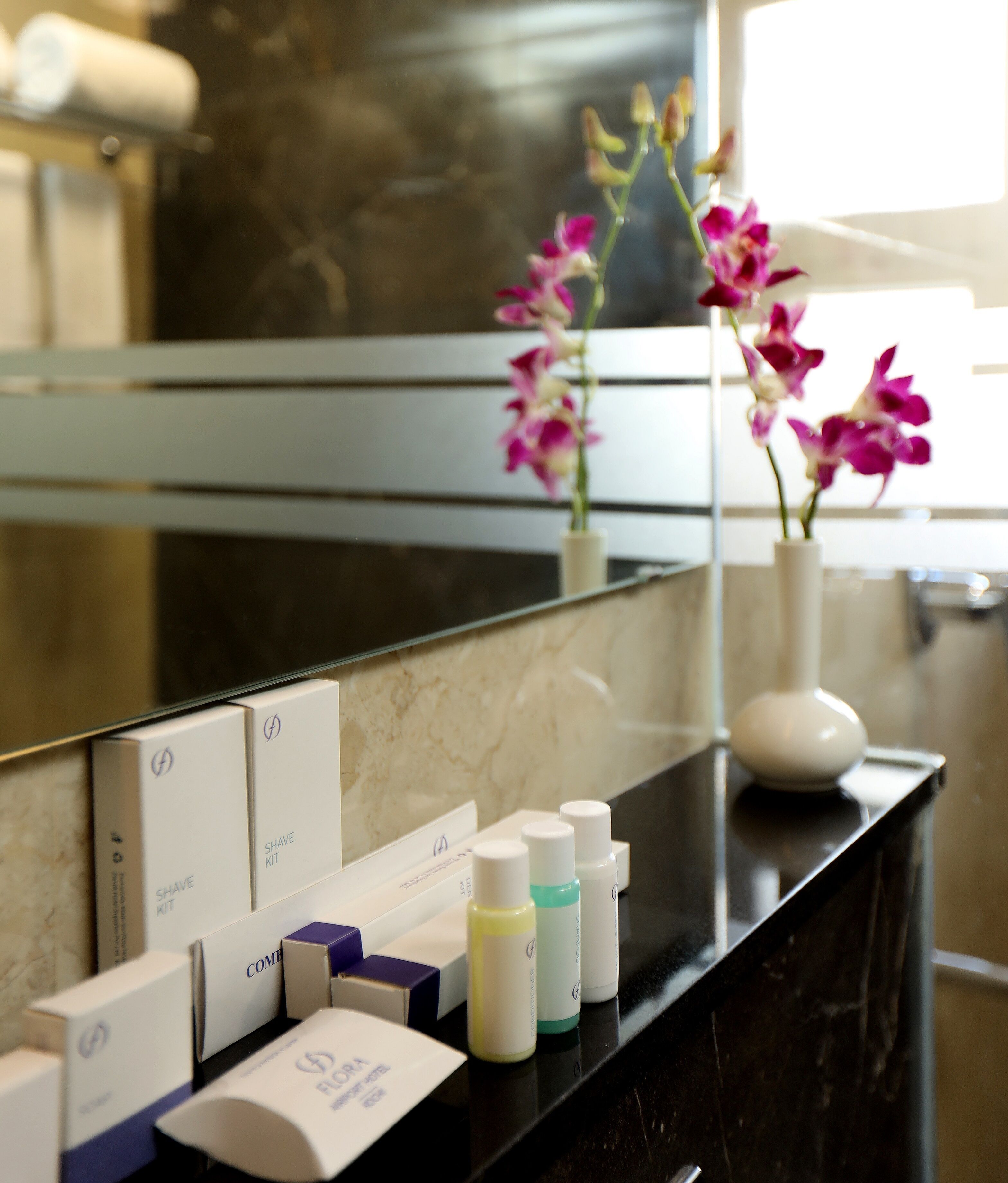 A bathroom vanity with a mirror, toiletries, and a vase with orchids.