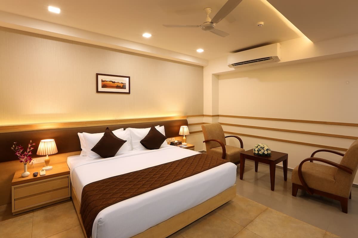 A hotel room with a large bed, a nightstand with a lamp, a chair, and a small table with flowers.